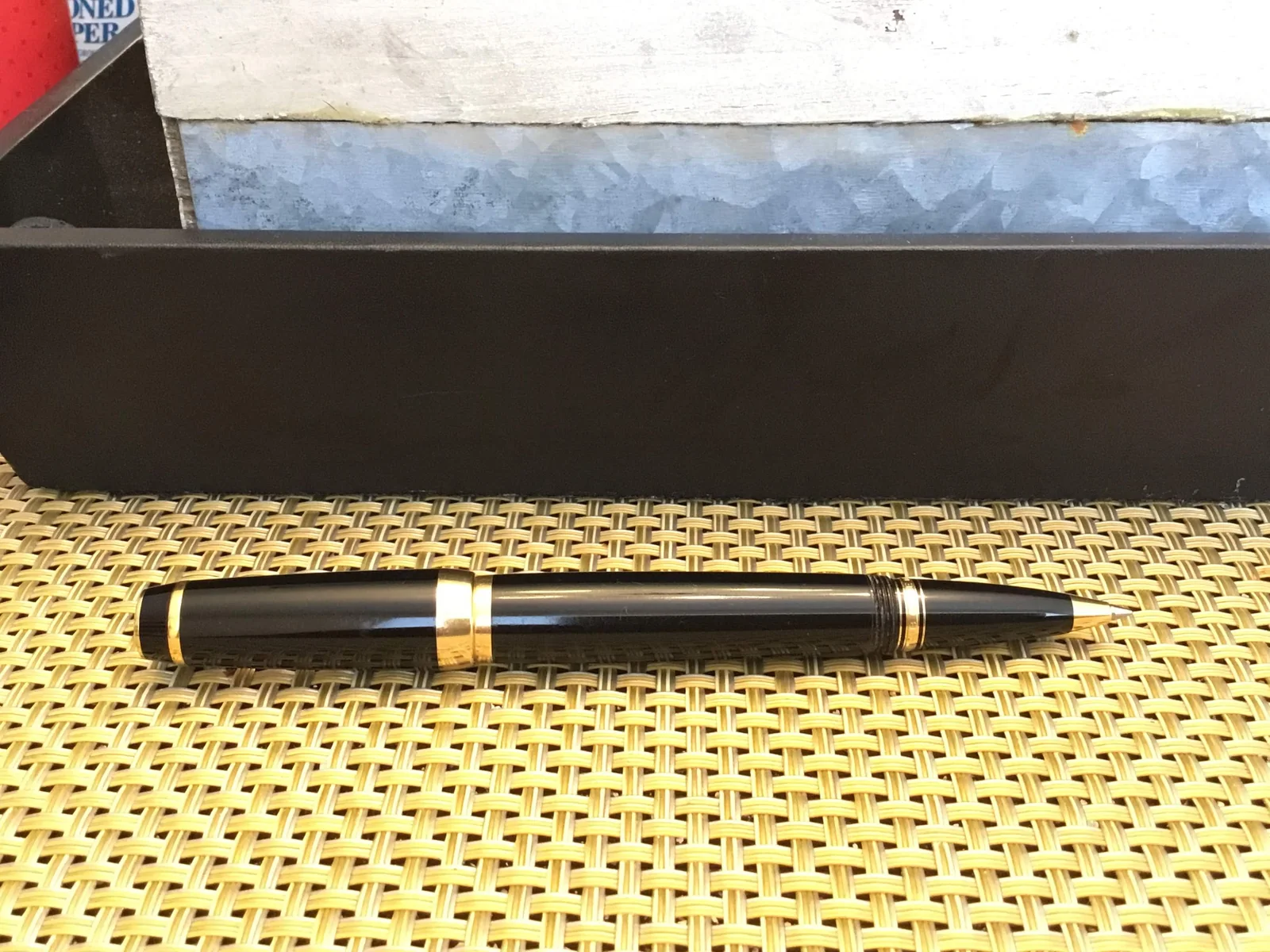 Black fountain pen with gold-tone trim shown horizontally on a woven surface